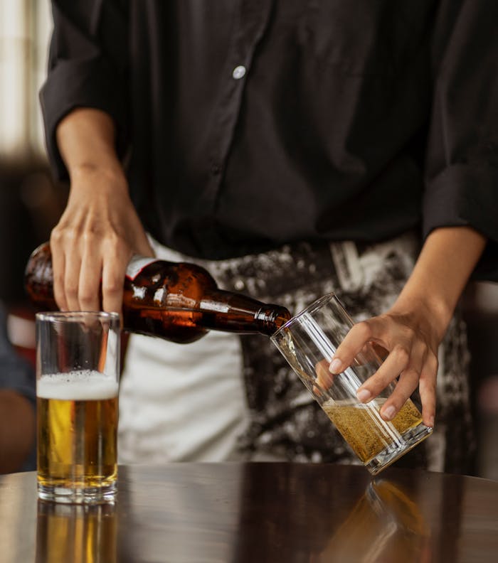Person pouring beer from a bottle into a glass on a table in a relaxed indoor setting.